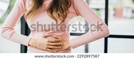 Sick woman unhappy having stomach ache at home, Asian young female suffers from stomachache after eating spoiled food, Abdominal pain from menstrual cramps Royalty-Free Stock Photo #2292897587