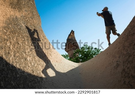 Tourist taking picture in Cappadocia in Pasabag Monks Valley, Man standing on u shaped rock formation detail, Shadow of man on cliff, Goreme National Park, Travel in Turkey Central Anatolia