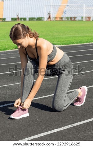 Young woman hands tie laces on her pink sport shoes on a stadium, ready for running, sport and fitness concept.