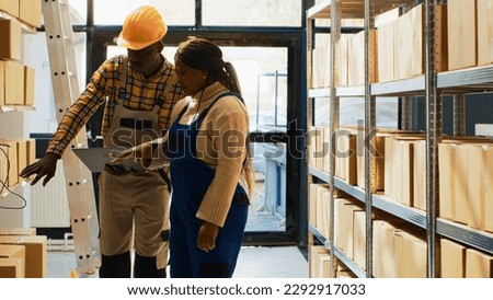 African american people using laptop to do inventory, looking at merchandise in cardboard packages on racks. Man and woman working in storage room to check stock and products.