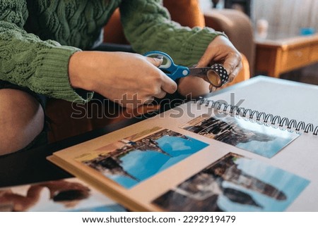 Hands of an unrecognizable middle-aged woman cutting a piece of washi tape to paste some photos into her handmade kraft travel paper album. Royalty-Free Stock Photo #2292919479