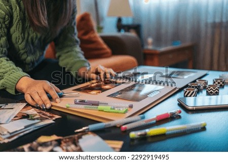 Unrecognizable middle-aged woman sitting on her living room sofa checking the condition of her handmade kraft travel album with washi tape. Royalty-Free Stock Photo #2292919495