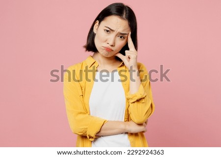 Young sad upset dissatisfied woman of Asian ethnicity wears yellow shirt white t-shirt look camera prop up forehead isolated on plain pastel light pink background studio portrait. Lifestyle concept Royalty-Free Stock Photo #2292924363