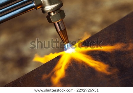 Gas cutting of metal. Gas cutter with copper nozzle with a stream of fire directed at the metal. Heating up the metal with a gas cutter. Royalty-Free Stock Photo #2292926951