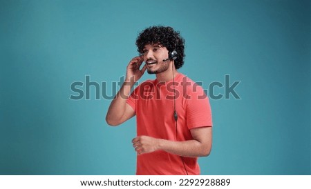 latin spanish male call center operator with head set talking in coral t-shirt on blue studio background. Royalty-Free Stock Photo #2292928889