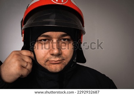 close-up portrait of a handsome firefighter in a helmet and gear, on a gray background and looking at the camera. Concept of saving lives, heroic profession, fire safety