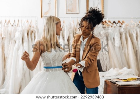 Tailor is measuring waist circumstance on a beautiful bride in a bridal salon