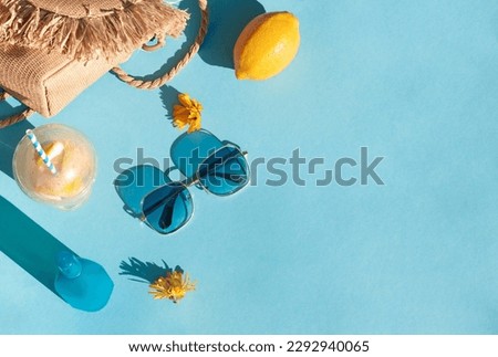 Bright summer beach vacation or travel lifestyle concept frame with lemonade, a straw bag, sunglasses and sunscreen spray. Top view. Copy space