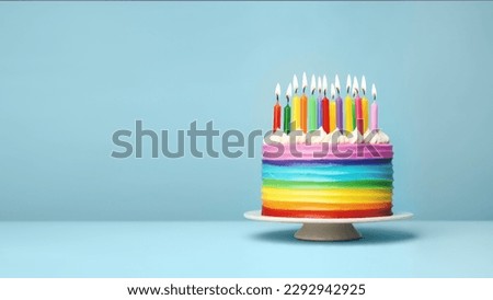 Colorful rainbow birthday cake with colorful rainbow birthday candles for a party, blue background with copy space