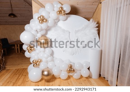 A luxury arch for a child's birthday in a restaurant. Photo zone with golden balloons and white angel wings with letters. Photo zone for the celebration