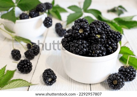 Organic blackberry with green leaf in a plate on a white rustic wooden background