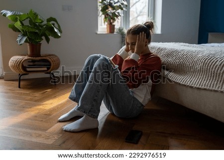 Frustrated sad teen girl child sitting alone on floor being bullied online, having feelings of isolation and fear. Depressed teenage kid holding head in hands dealing with first love heartbreak Royalty-Free Stock Photo #2292976519