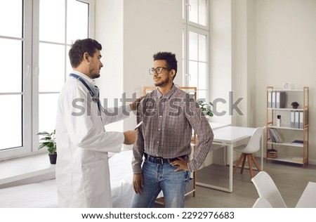 Medical ethics and health care. Male doctor touches patient's shoulder for encouragement and support before medical examination. Doctor assures young dark-skinned man that everything will be fine. Royalty-Free Stock Photo #2292976683