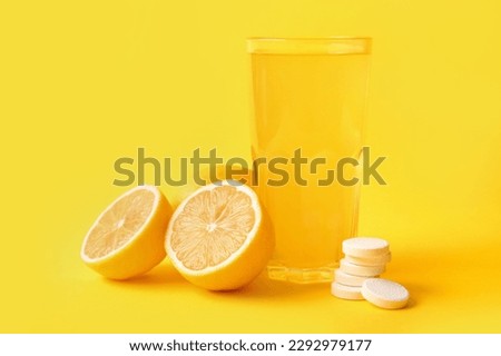 Glass of vitamin C effervescent tablet dissolved in water and lemons on yellow background