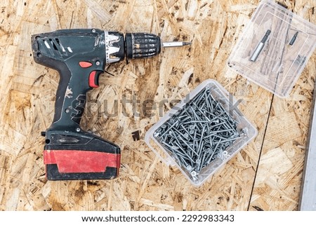 An electric screwdriver, a box of screws and bits are lying on the surface of the OSB plate