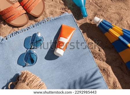 Bright summer beach vacation or travel lifestyle concept with sunscreen cream, sunglasses, sun umbrella and flip flops on the sand. Top view.  Royalty-Free Stock Photo #2292985443