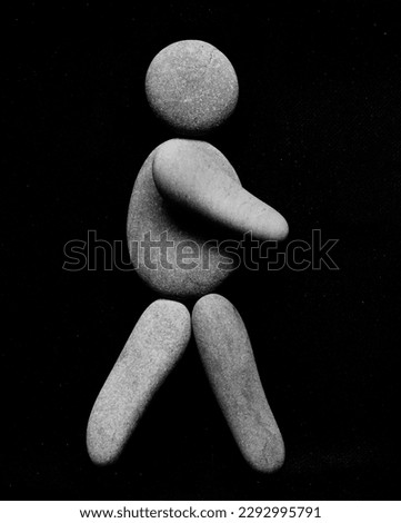 human figure walking with hands  isolated on black background. female or Male symbol made from many pebbles. grey round stones in the form of man or woman.