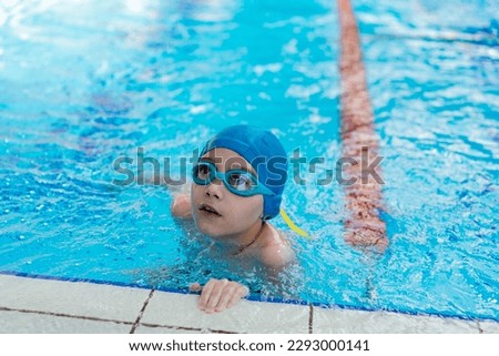 little caucasian boy wearing goggles looking out from swimming pool. High quality photo with selective focus