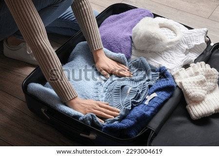 Young woman unpacking her warm clothes from suitcase on wooden floor, closeup