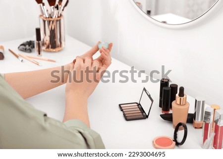 Woman applying perfume on wrist at dressing table indoors, closeup