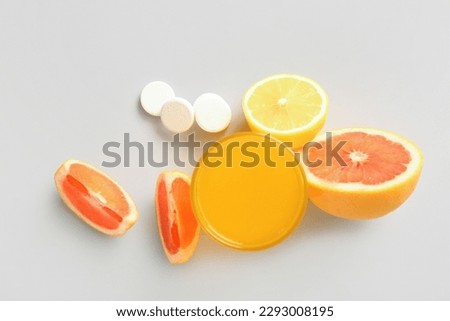 Glass of vitamin C effervescent tablet dissolved in water and fruits on grey background