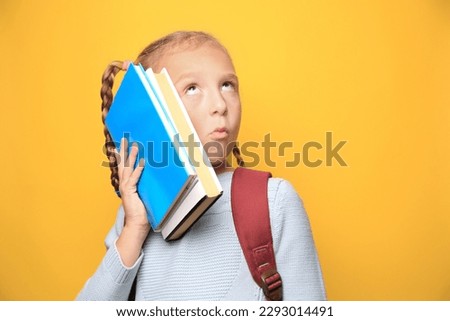 Funny little girl with backpack and textbooks on yellow background. Space for text