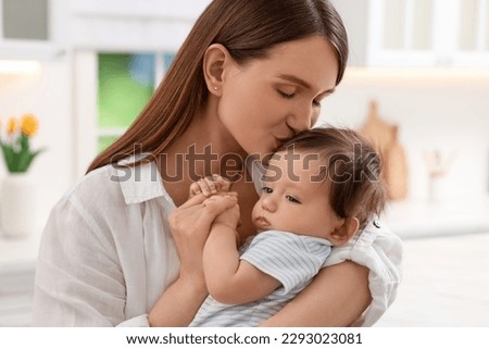 Happy mother kissing her little baby in kitchen