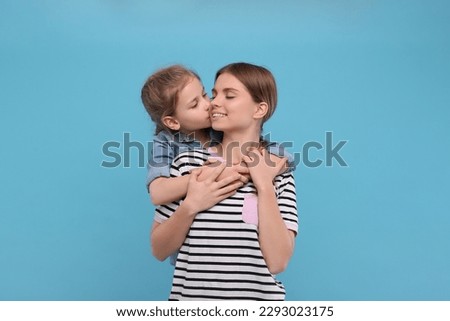 Little daughter kissing her mom on light blue background. Happy Mother's Day