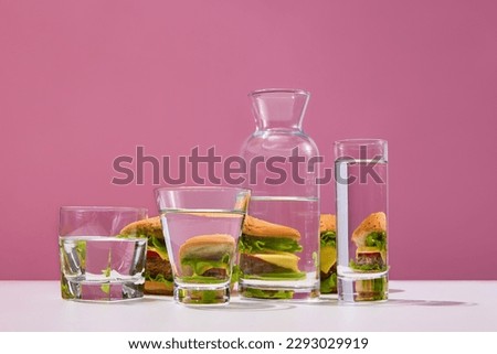 Fast food addiction. Still life with a lot of fresh, delicious burgers near the water glasses over pink studio background. Concept of food restrictions, diet, fat, carbs, junk food, unhealthy food Royalty-Free Stock Photo #2293029919