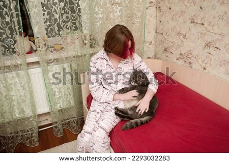 A girl in sleeping clothes sits on a bed and hugs her pet, a Scottish fold cat. An image about attitude and love for pets.