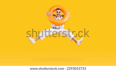 Full body photo of a happy funny man in sunglasses holding rubber ring and jumping isolated on studio yellow background. Funny tourist is going on summer holiday trip. Vacation and travel concept.