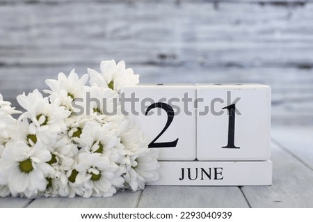 Summer Solstice White wood calendar blocks with the date June 21st  and white daisies. Selective focus with blurred background. 