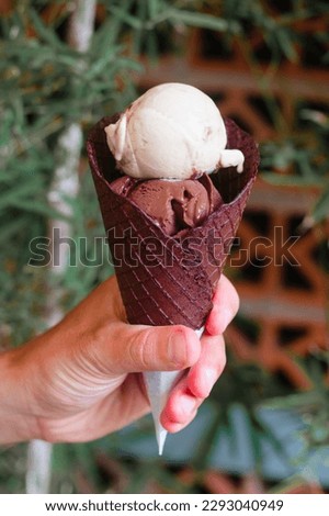 A man's hand holds a cone with delicious ice cream. Natural chocolate dessert with vanilla. Cooling gelato in summer in the heat