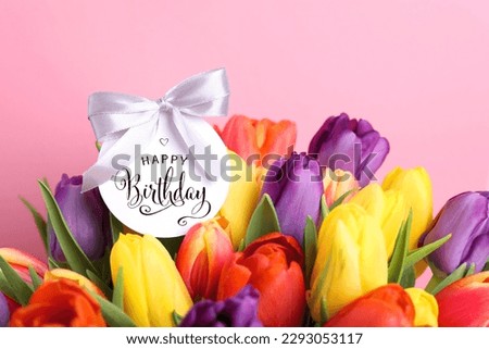 Beautiful bouquet of tulip flowers with Happy Birthday card on pink background, closeup