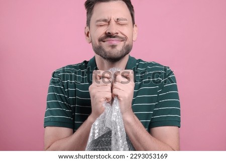 Man popping bubble wrap on pink background, closeup. Stress relief