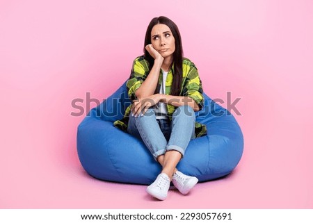 Full length photo of upset bored woman dressed plaid shirt sitting bean bag looking empty space isolated pink color background