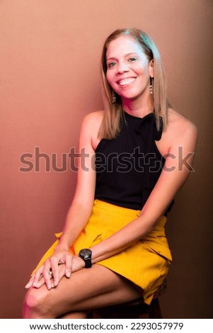Portrait of smiling, happy woman wearing black and yellow, isolated on brown background.