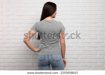 Woman wearing stylish gray T-shirt near white brick wall, back view