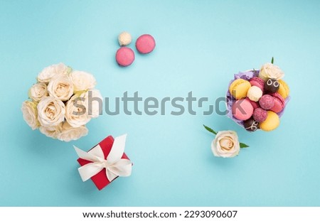 Sweet cookies macaroons, red gift box, rose flowers and chocolate candies on blue background. Spring presents concept for Mothers day, womans day, birthday. Flat lay, empty space for text or message
