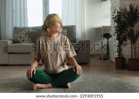 Young woman with cancer taking yoga and meditating in her apartment.