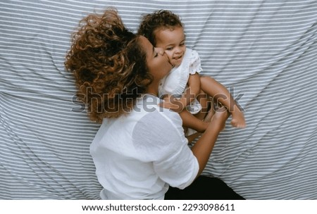 Enjoying free time together. Happy young African American mother and daughter having fun and kissing lying on bed together. Black Family holiday and togetherness, Love emotion.