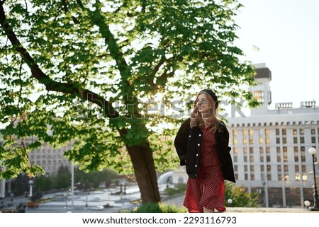 Fashion portrait of stylish elegant lady with urban background at sunset. Attractive blonde young caucasian girl in beret, jacket and polka dot red dress going in the city center. High quality image