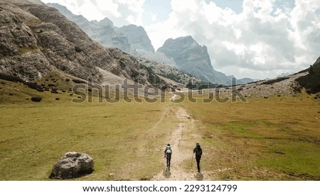 A couple hiking along a pathway leading through a valley in Italian Dolomites. High, sharp mountains around. Stony and raw landscape, green meadow. Remote and desolate place. Freedom of exploration Royalty-Free Stock Photo #2293124799