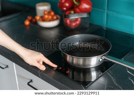 cropped shot of female hand press button on control panel of induction stove and choose temperature for cooking in frying pan at home kitchen Royalty-Free Stock Photo #2293129911