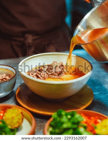 Unknown chef pouring broth into a chicken soup with meat and vegetable. Pho bo