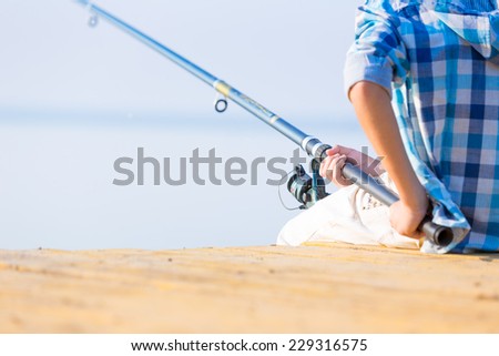 Close-up of hands of a boy with a fishing rod that is fishing on the pier