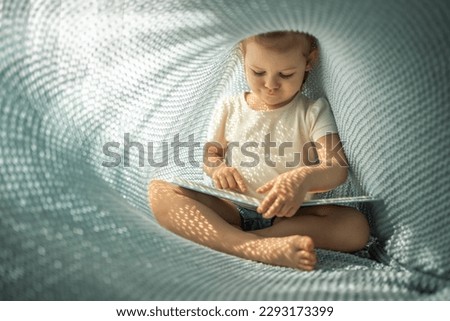 Little girl enjoying of review a book under blue knitted plaid in sunny morning. High quality photo