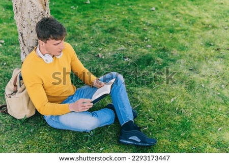 High angle side view of young man and woman reading book while sitting on grass in park Royalty-Free Stock Photo #2293173447