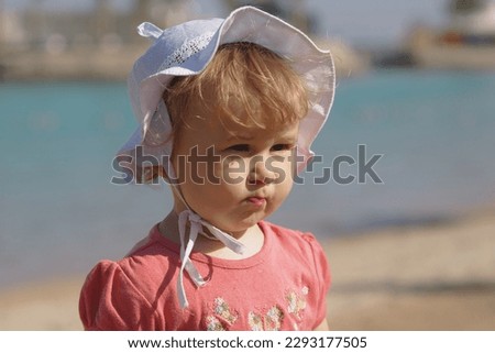 Little girl on the background of the sea, in a white panama hat with a dissatisfied thoughtful expression, summer family vacation