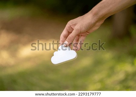 Man holding a simple white cloud symbol in hand, cloud computing and storage services sign held in hand, object isolated, blurred background, copy space. Cloud technology, AI computation, storing data